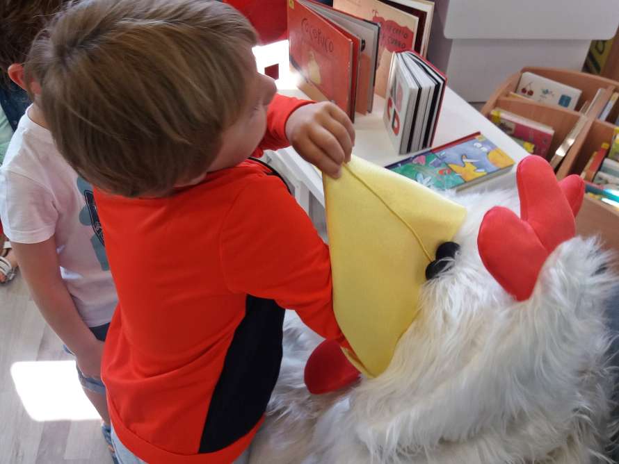 niño jugando con gallina de peluche y libros al fondo