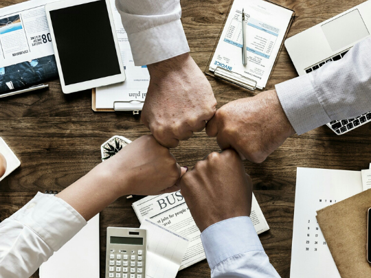 Cuatro manos chocando los puños sobre mesa de trabajo