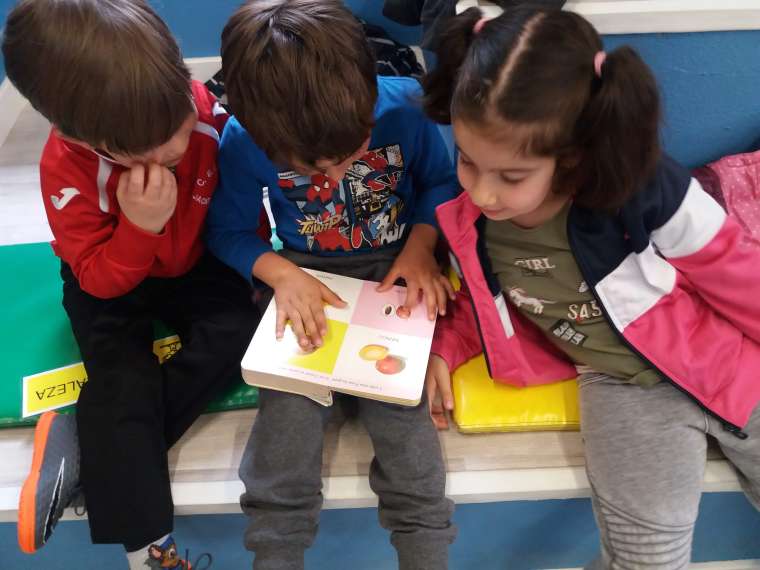 dos niños y una niña leyendo juntos un libro en espacio infantil
