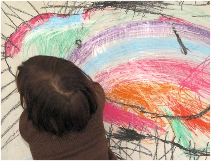Imagen de un niño o niña de espaldas junto a un dibujo abstracto que parece haber dibujado él.