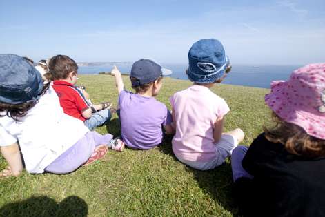 Varios niños y niñas sentados de espaldas sobre un prado.