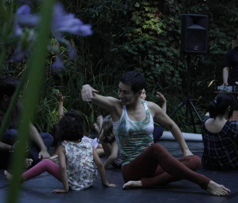 Una monitora enseña a una niña, sentadas ambas en el suelo, movimientos de baile.