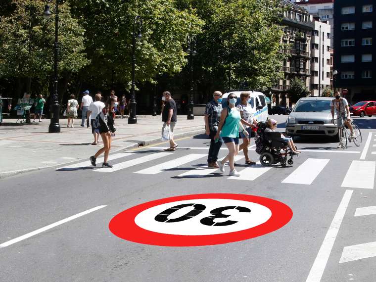 Varias personas cruzan la calle por un paso de cebra junto a una señal horizontal de límite 30.