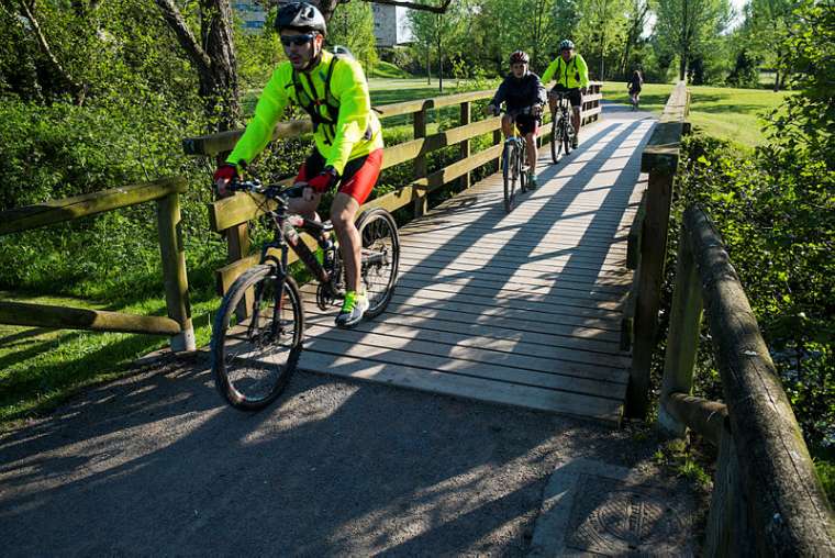 Tres personas cruzan en bicicleta a través de un puente de madera de la senda del río Piles.