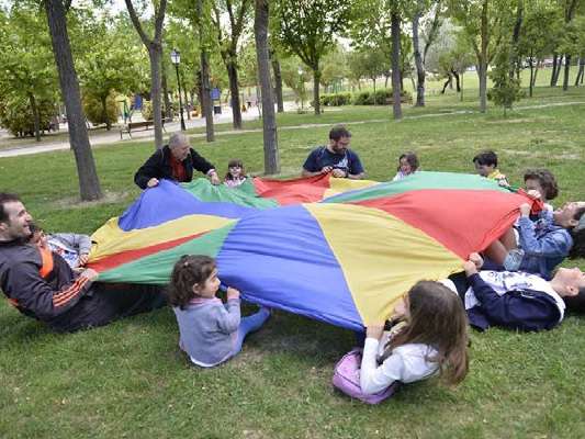 Niños, niñas y sus respectivos padres juegan en el prado del parque de Isabel La Católica.