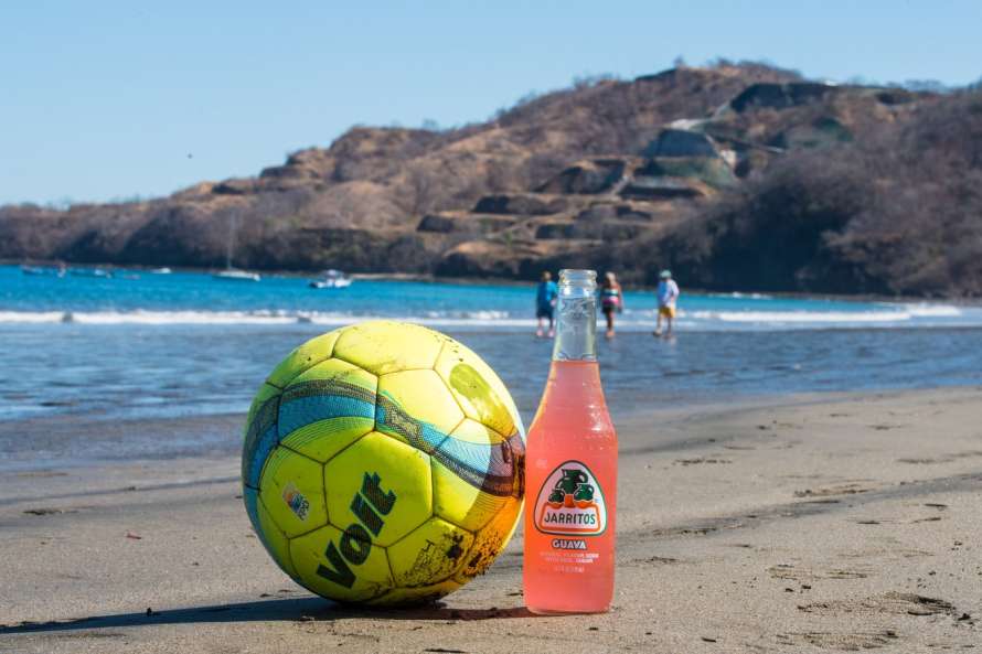 Balón y refresco en la arena de una playa.