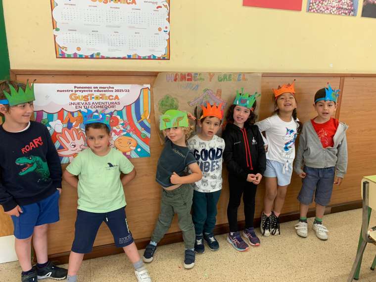 Grupo de siete niños y niñas con coronas de cartulina de colores en sus cabezas. Están en un aula 