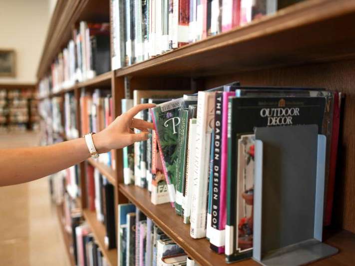 brazo de una persona cogiendo un libro de una estanteria