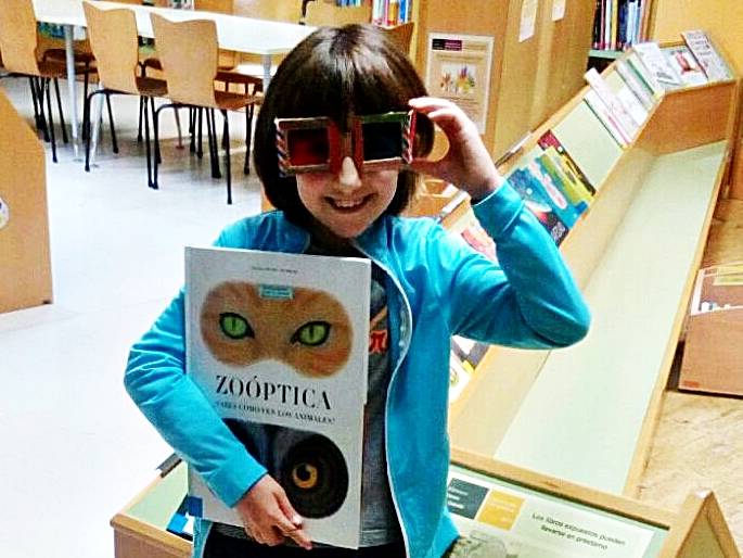 niña con gafas de sol y libro en la mano en la bibliotecac